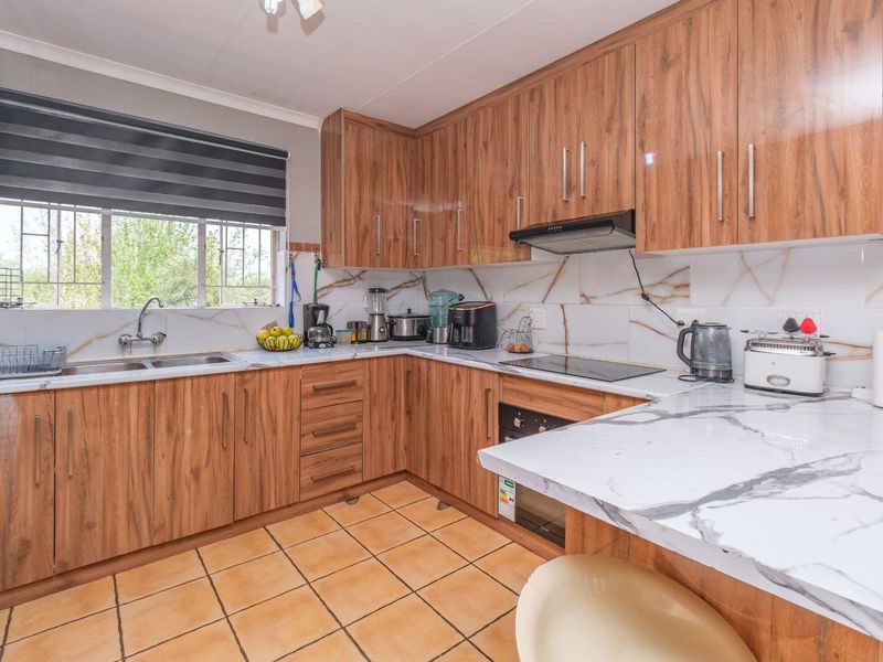 A functional kitchen featuring wood-look cabinetry, marble-effect countertops, a built-in oven with hob, and a double stainless steel sink.