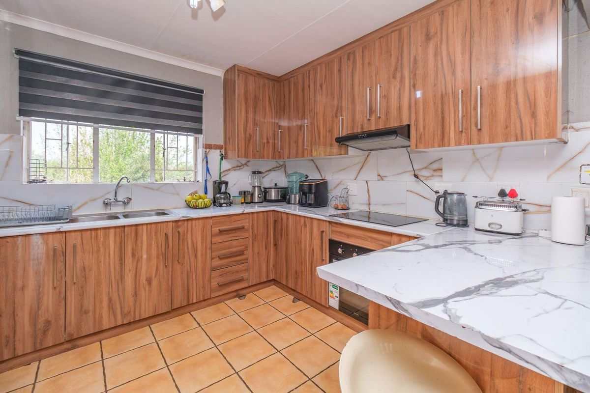 A functional kitchen featuring wood-look cabinetry, marble-effect countertops, a built-in oven with hob, and a double stainless steel sink.