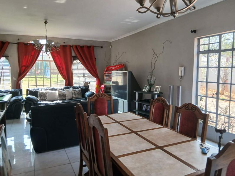 Spacious open-plan living and dining area featuring tiled flooring, large windows with natural light, and classic chandelier lighting fixtures.