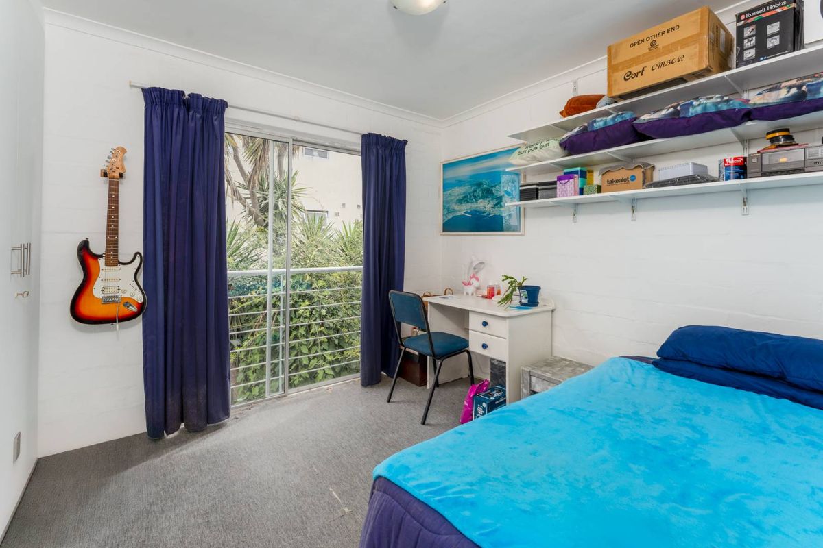 A bedroom featuring carpeted flooring, built-in wall shelving, and a sliding glass door providing access to a balcony with greenery views.