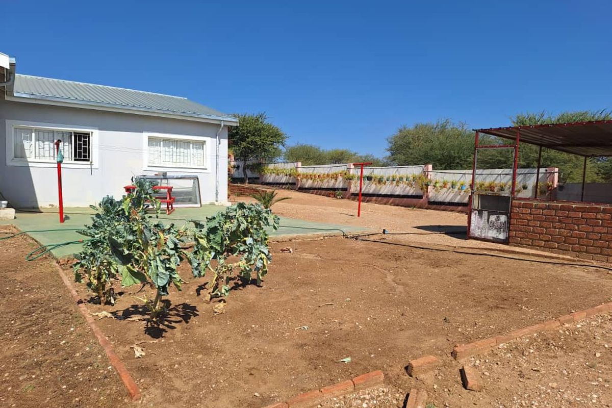 A spacious rear garden area featuring a paved patio section, a vegetable patch, and a covered outdoor structure with a brick base.