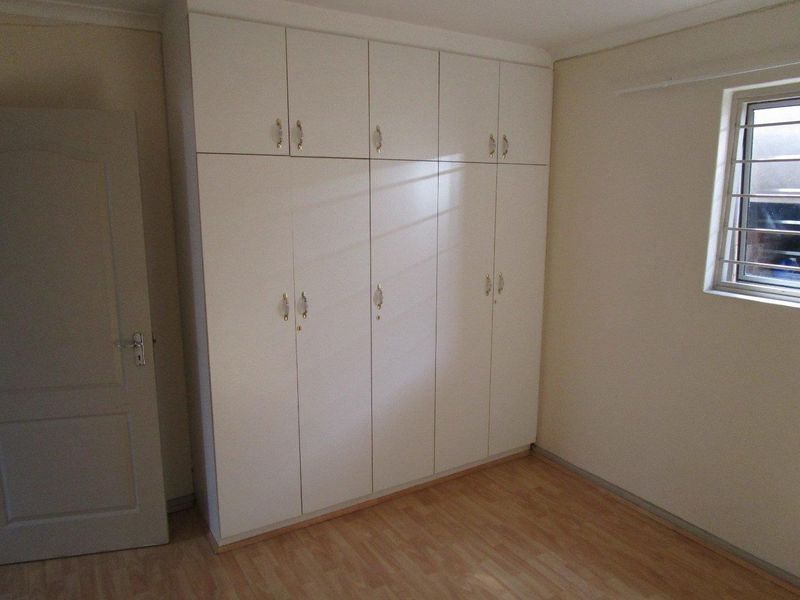 A clean, empty bedroom featuring light-toned laminate flooring and floor-to-ceiling built-in cupboards, providing ample storage space.