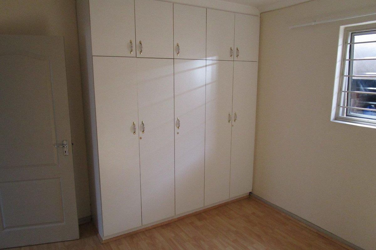 A clean, empty bedroom featuring light-toned laminate flooring and floor-to-ceiling built-in cupboards, providing ample storage space.