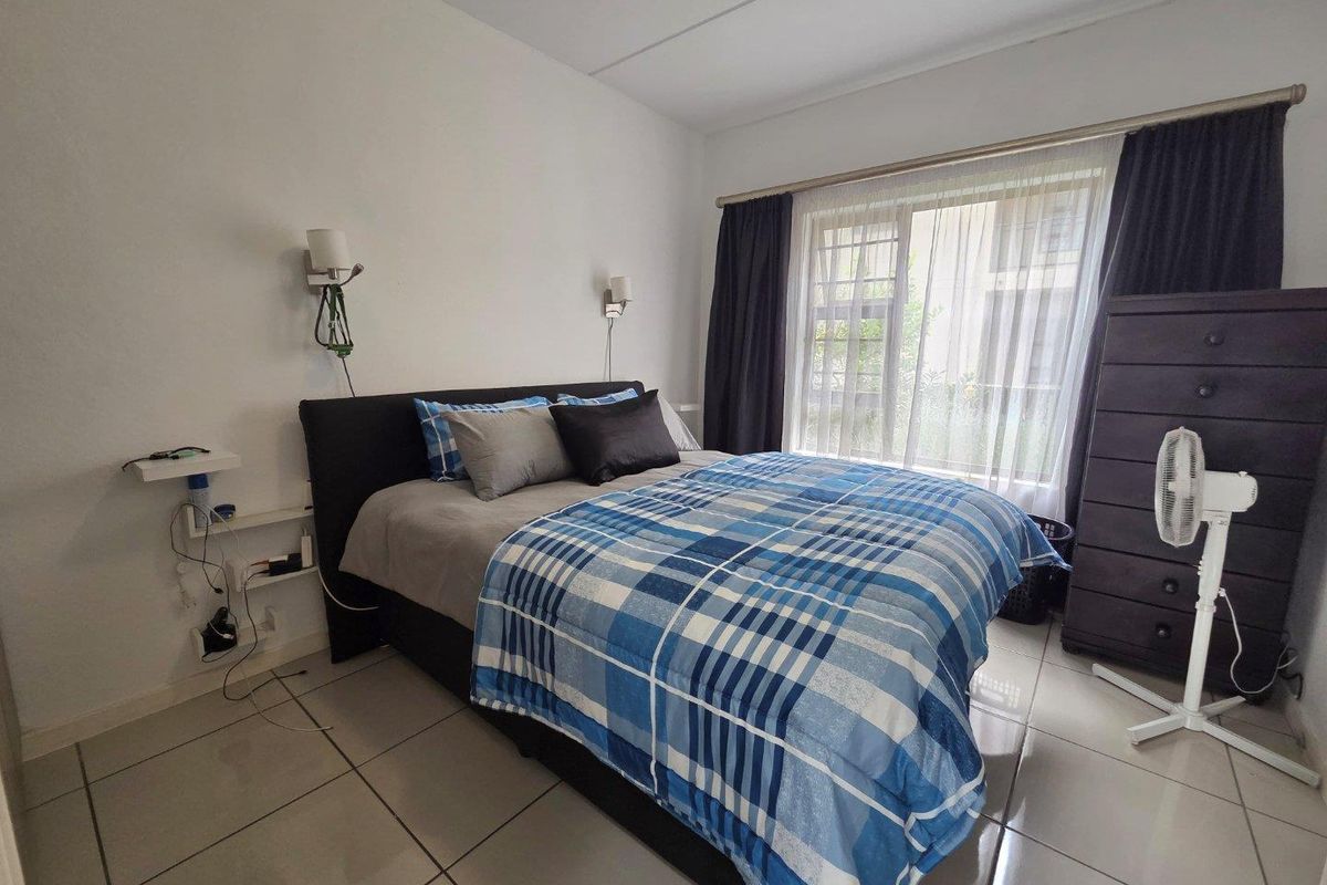A bedroom featuring tiled flooring, wall-mounted bedside lighting, and a large window with curtain tracks, providing natural light and access to the exterior.