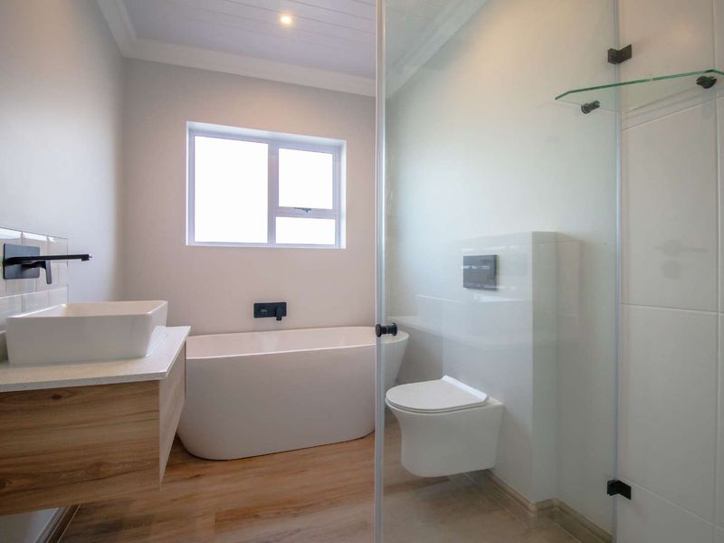 Modern bathroom featuring a sleek freestanding bathtub, wall-mounted toilet, vessel sink vanity, and a glass-enclosed shower with contemporary black fixtures.