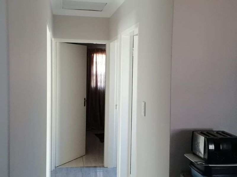 A simple interior hallway connecting multiple rooms, featuring neutral wall finishes and a ceiling access hatch.
