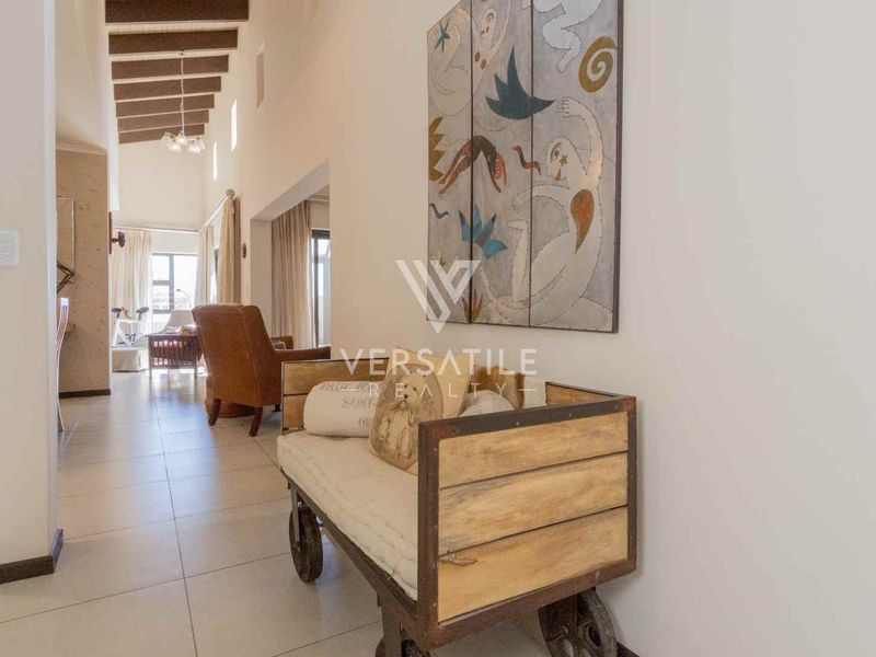 Spacious hallway featuring double volume ceilings with exposed timber beams and neutral tiled flooring, leading into the main living area.