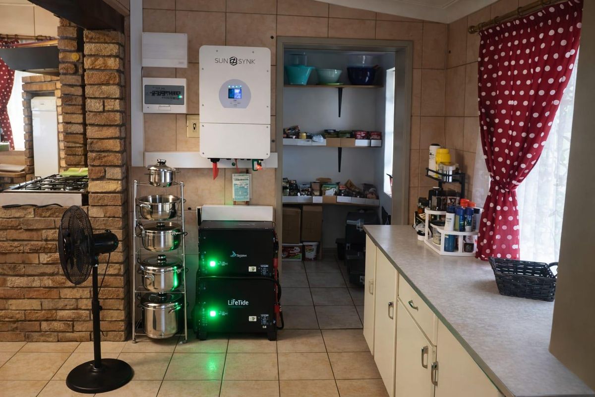 A functional kitchen area featuring a built-in solar inverter and battery storage system, adjacent to a walk-in pantry with shelving.