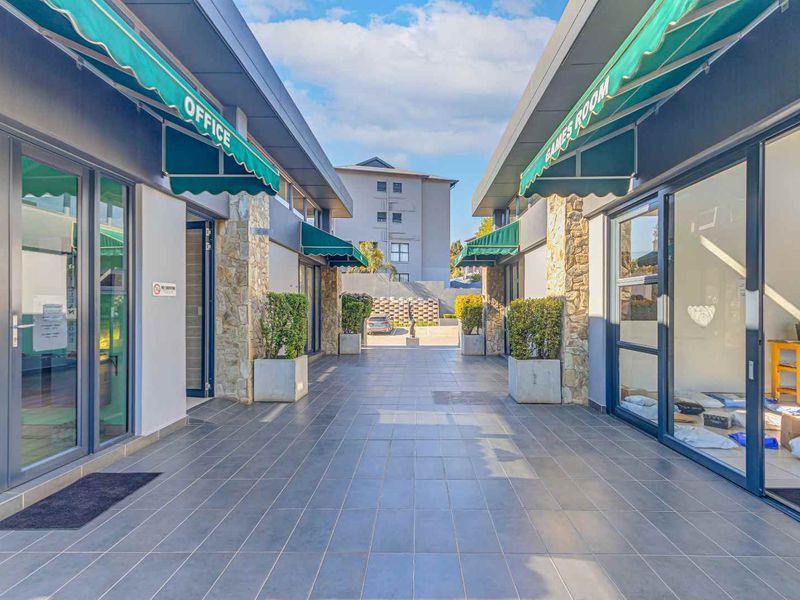 A well-maintained outdoor walkway between building wings featuring stone-clad pillars, tiled flooring, and green retractable awnings leading to a communal office and games room.