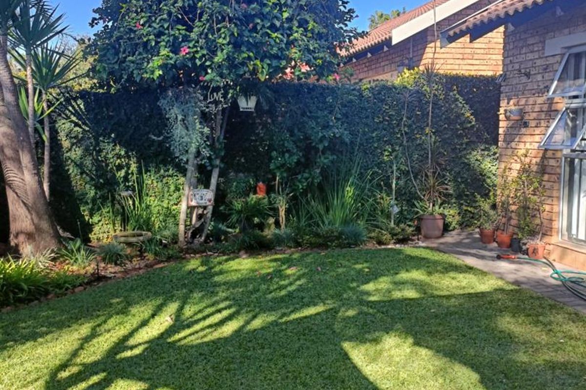 A well-maintained rear garden featuring a lush lawn, mature trees, and a brick townhouse facade with paved access.