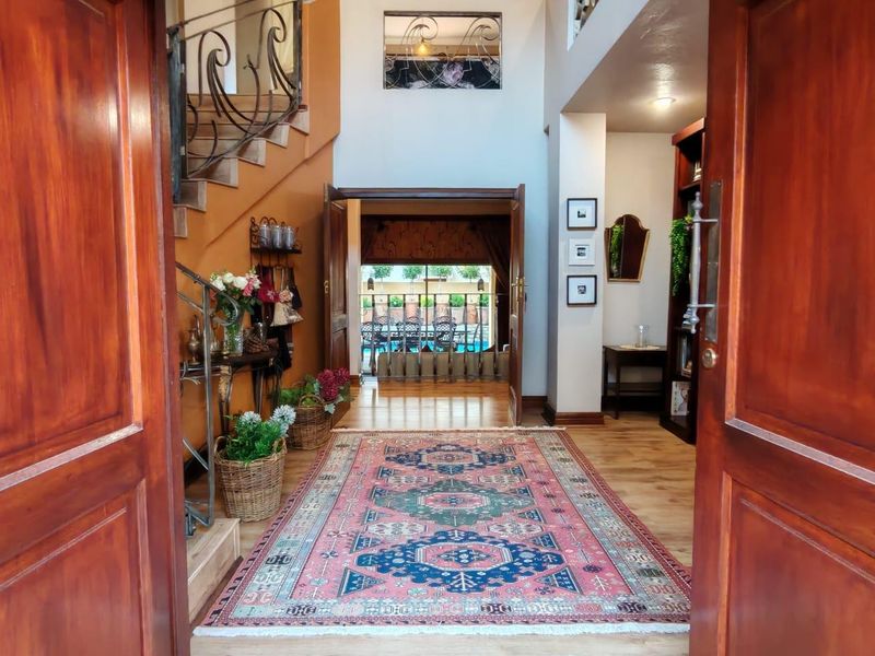 Welcoming double-volume entrance hall featuring a wrought iron staircase, warm wood-toned flooring, and a clear line of sight through to the rear patio area.