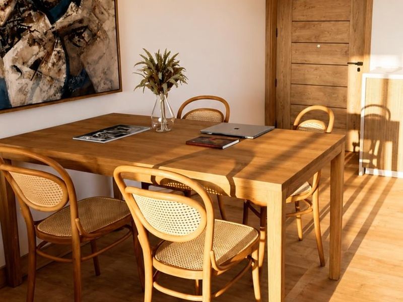 A bright dining area featuring warm wood-toned flooring and a solid timber door, illuminated by natural light.