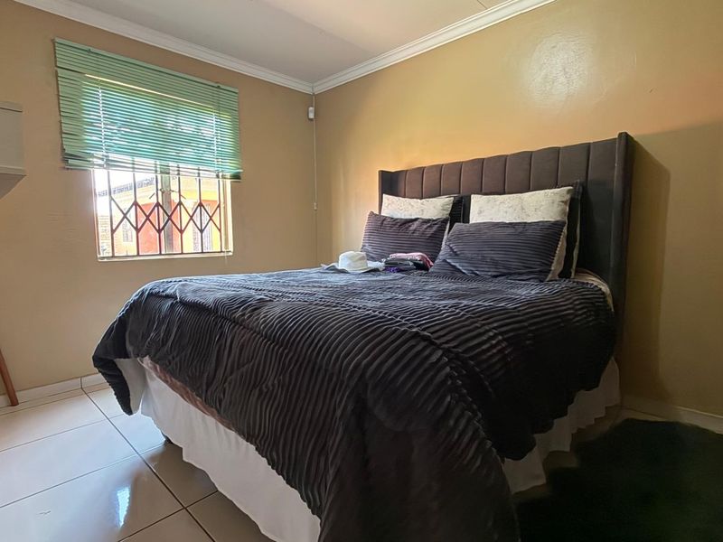 A bedroom featuring tiled flooring, crown molding, and a window fitted with security bars and venetian blinds.