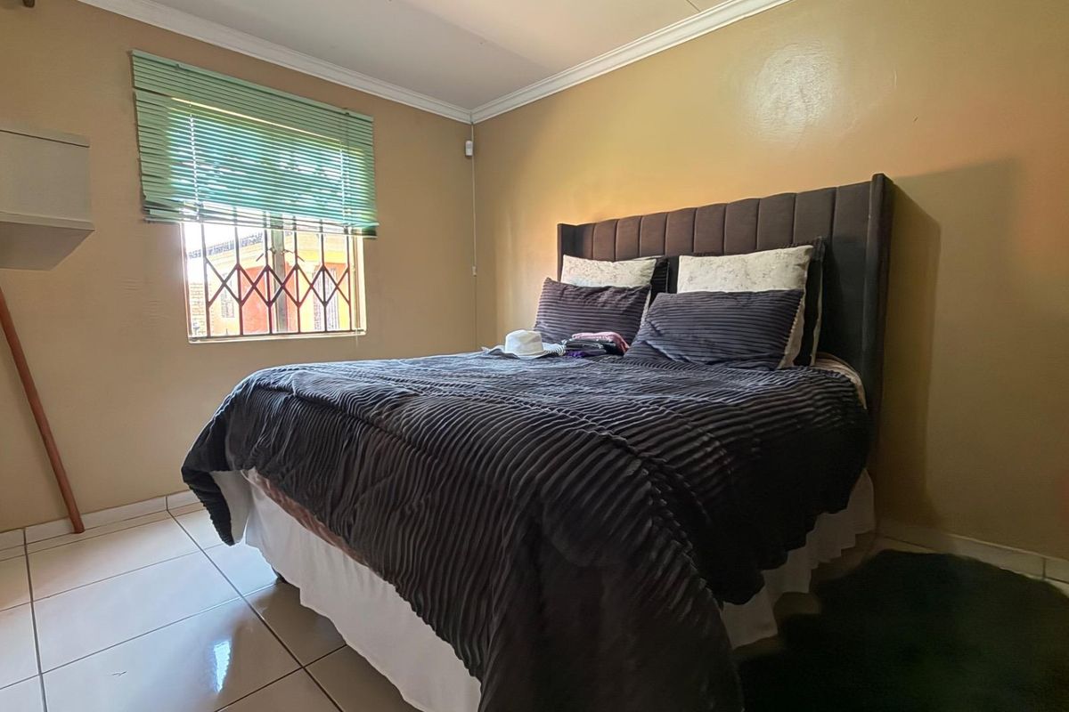 A bedroom featuring tiled flooring, crown molding, and a window fitted with security bars and venetian blinds.