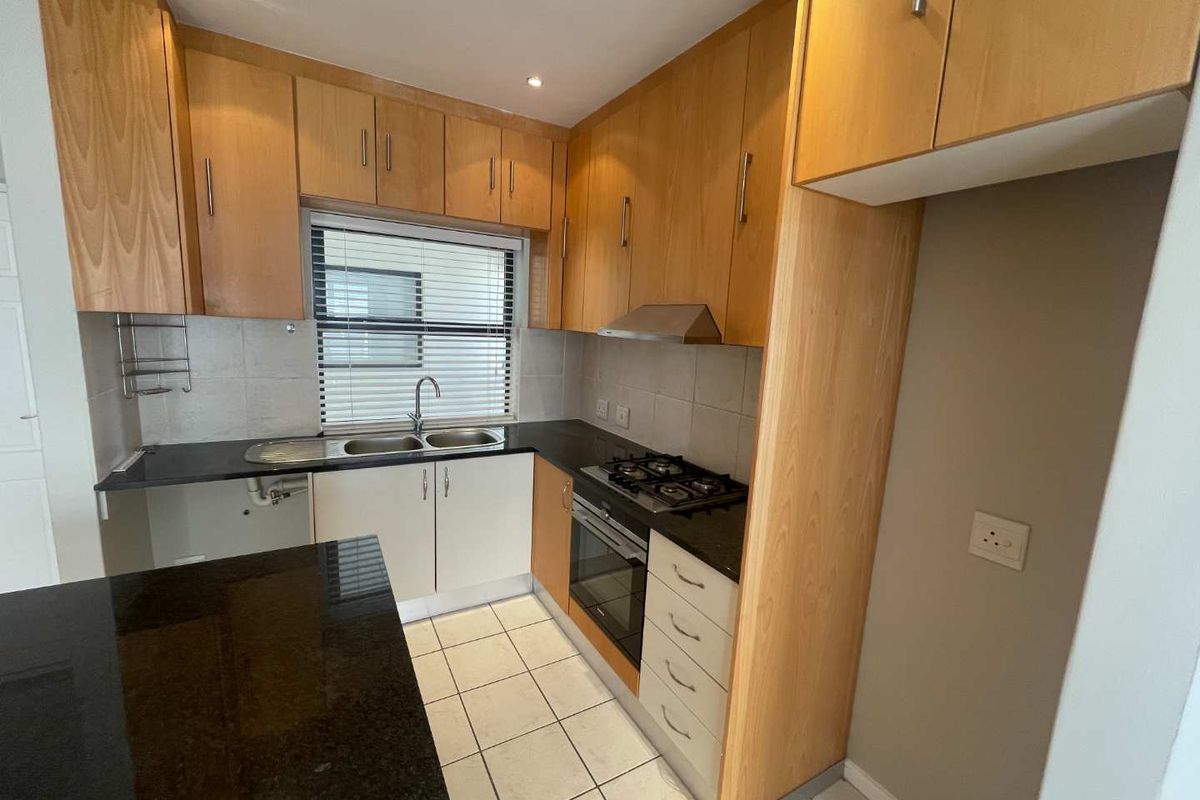 A functional kitchen featuring light wood cabinetry, granite countertops, a gas hob, and an integrated oven, with tiled flooring and recessed lighting throughout.