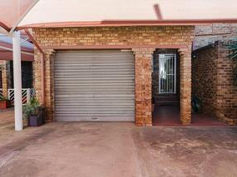 A brick-faced garage featuring a roller shutter door and an attached carport shade structure, providing secure parking for the townhouse.