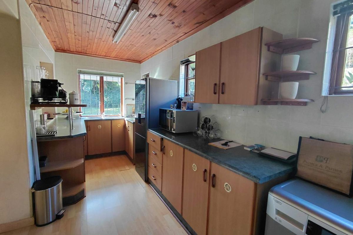 A functional kitchen featuring timber ceiling panels, laminate cabinetry, dark countertops, and tiled splashbacks with natural light from multiple windows.