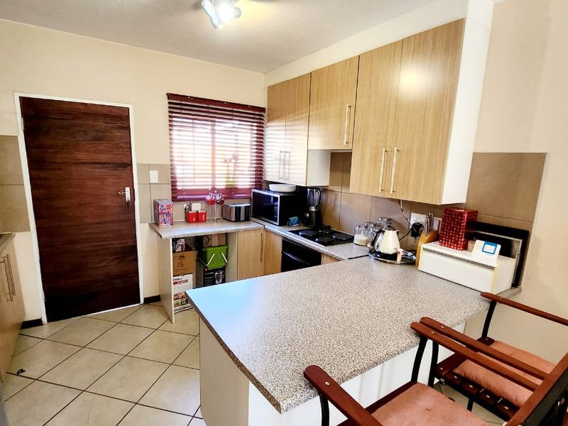 Functional kitchen featuring light wood-finish cabinetry, laminate countertops, tiled backsplash, and integrated oven and hob, with direct access to an adjacent area.