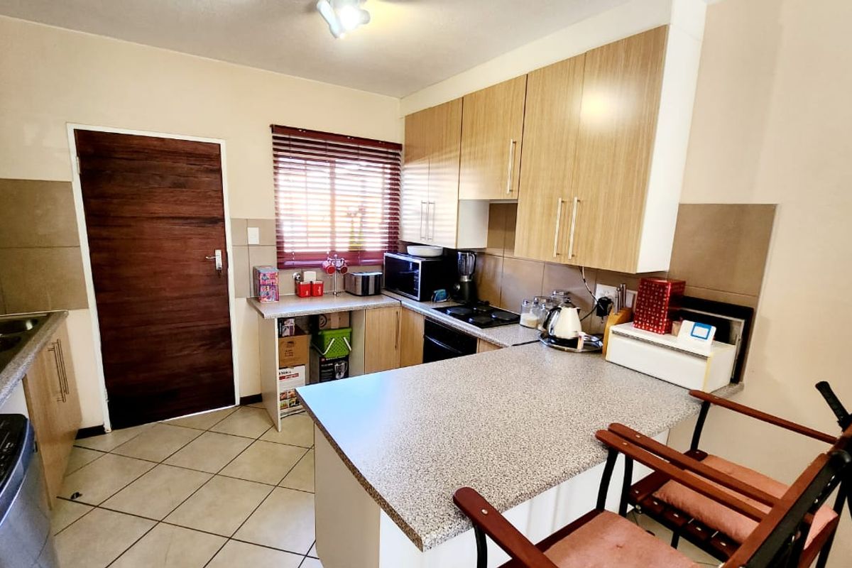 Functional kitchen featuring light wood-finish cabinetry, laminate countertops, tiled backsplash, and integrated oven and hob, with direct access to an adjacent area.
