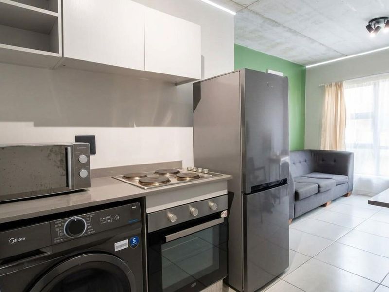 Modern open-plan apartment featuring a compact kitchen with built-in appliances, stone countertops, and an exposed concrete ceiling, flowing into a bright living area.
