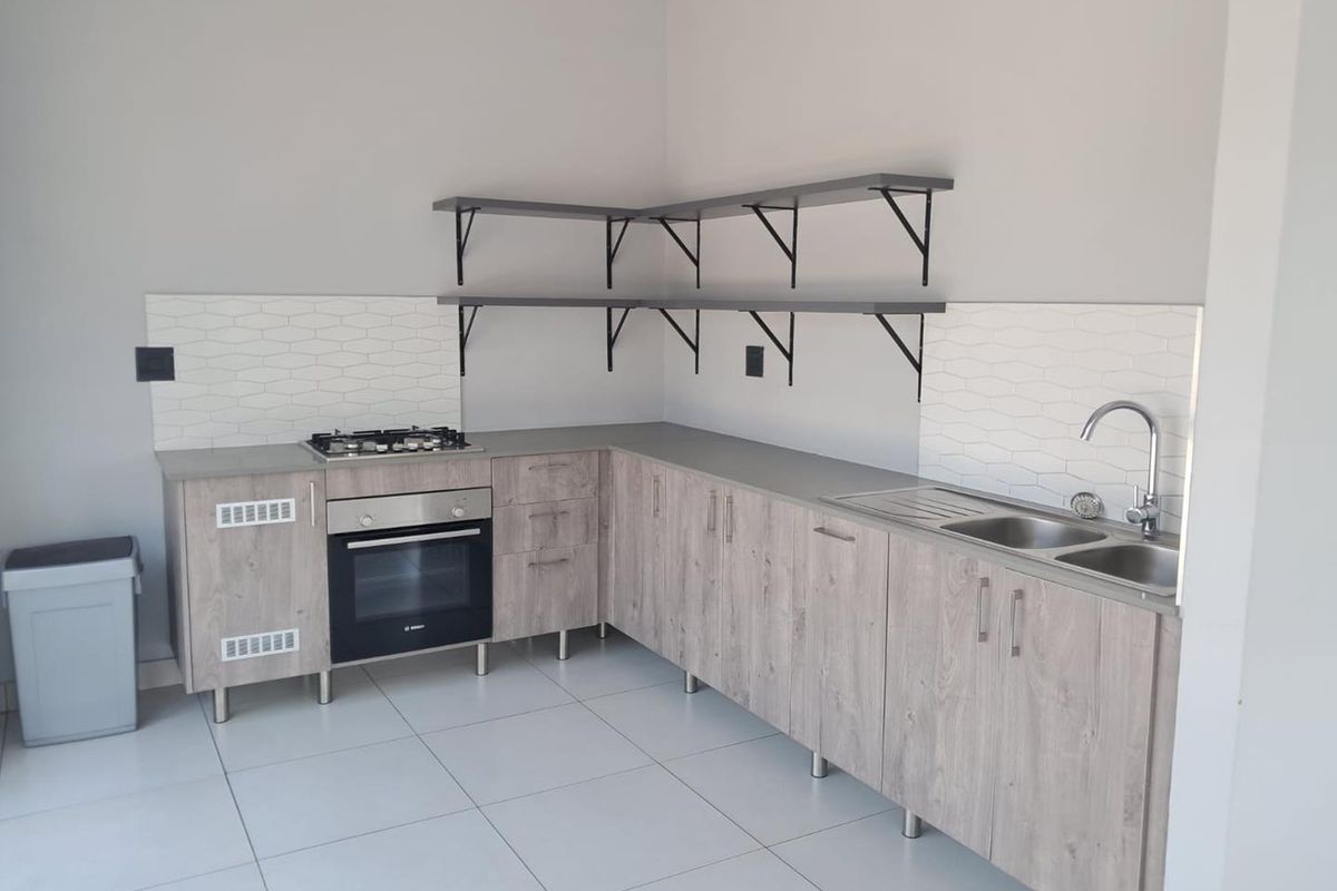 Modern kitchen featuring light wood-grain cabinetry, built-in oven, gas hob, stainless steel sink, and white hexagonal tile backsplash with open shelving.
