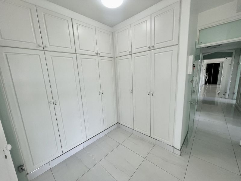 A bright hallway featuring extensive floor-to-ceiling built-in white cabinetry and clean tiled flooring, providing ample storage space.