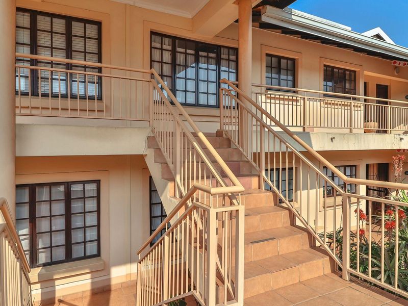Exterior view of an apartment complex featuring a central tiled staircase with metal balustrades and multi-pane windows on two levels.