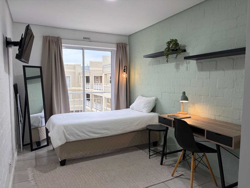 A well-lit bedroom featuring a textured accent wall, tiled flooring, and a sliding glass door providing access to a balcony.