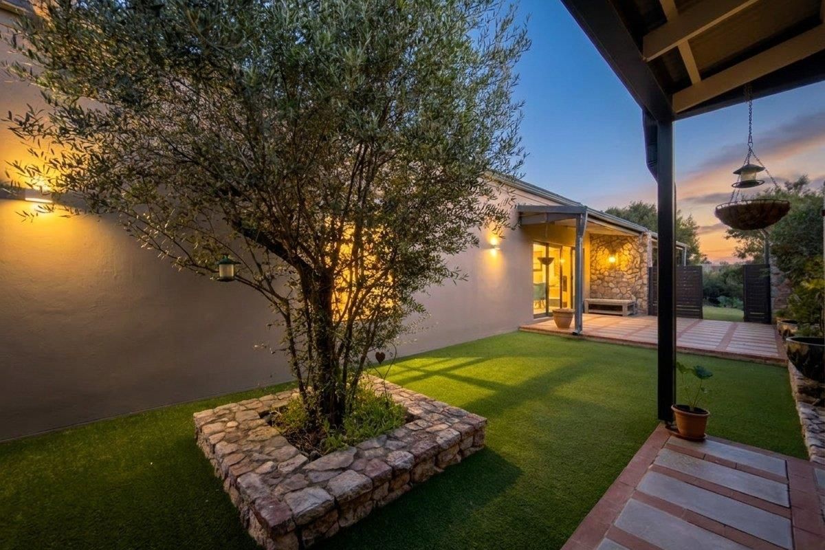 A well-maintained rear garden featuring a stone-clad planter, artificial lawn, and a covered patio area with stone wall accents.