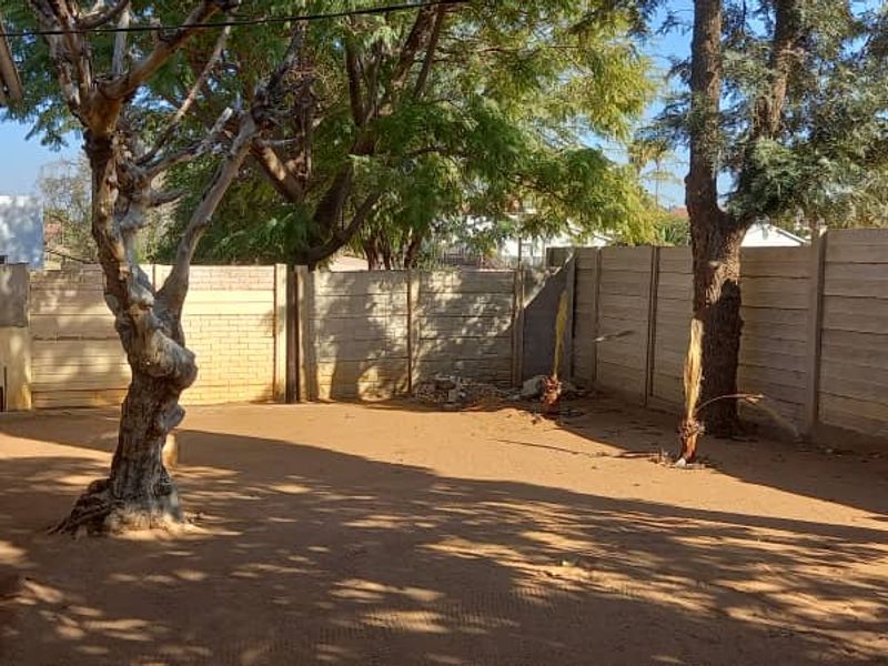 A rear yard area featuring a precast concrete boundary wall, mature trees, and an air conditioning unit mounted on the exterior wall.