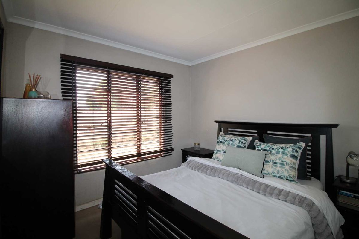 A well-maintained bedroom featuring neutral wall tones, fitted timber venetian blinds, and coved ceiling cornicing.
