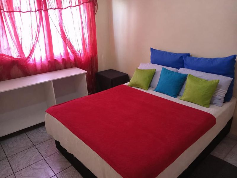 A bedroom featuring tiled flooring and a window with red curtains.
