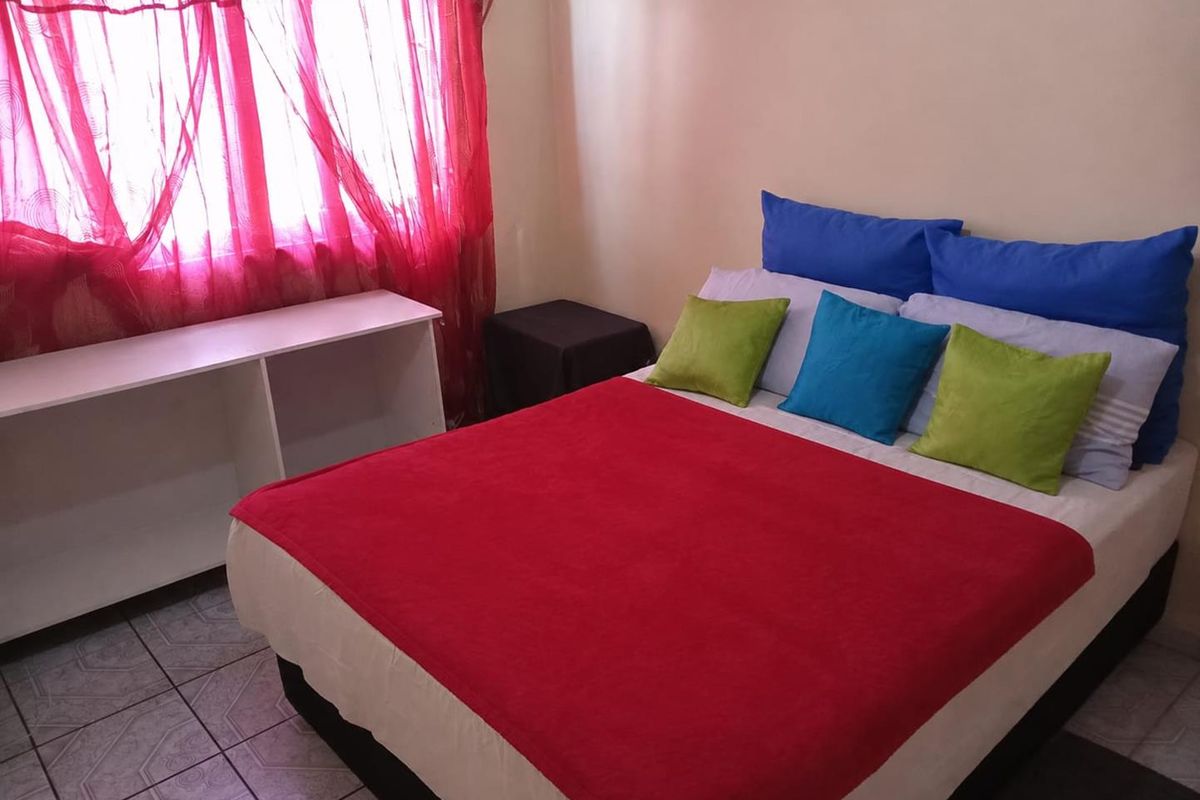 A bedroom featuring tiled flooring and a window with red curtains.