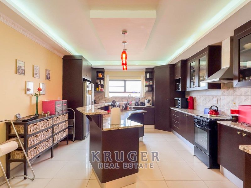 Spacious kitchen featuring dark wood cabinetry, granite countertops, tiled flooring, and integrated lighting with a central island layout.