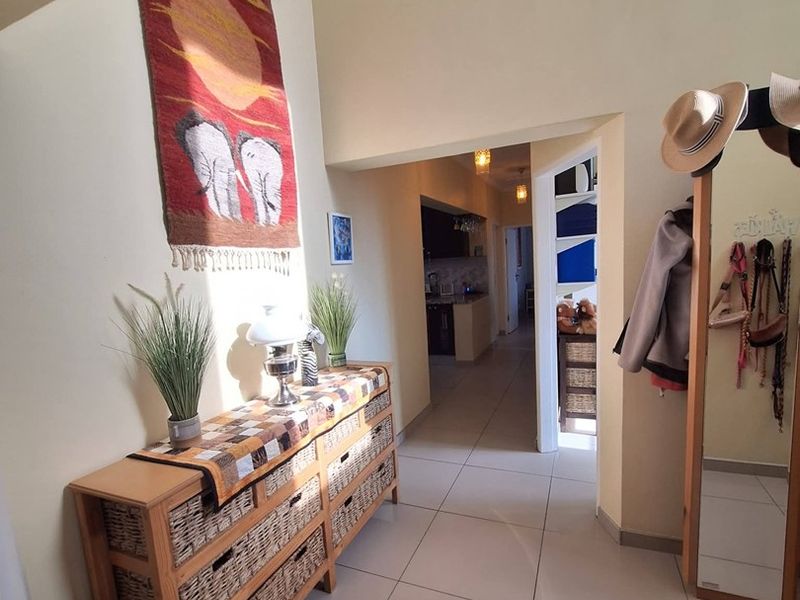 A bright and spacious hallway featuring neutral tiled flooring and high ceilings, providing a clear transition between the entrance and the kitchen area.