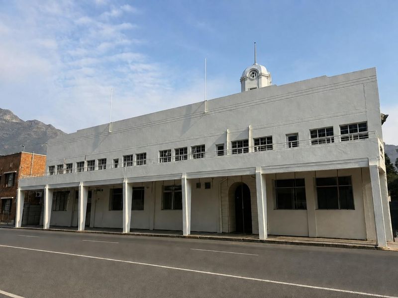 A historic mixed-use building featuring a prominent clock tower, covered ground-floor walkway, and classic architectural detailing along the street-facing facade.