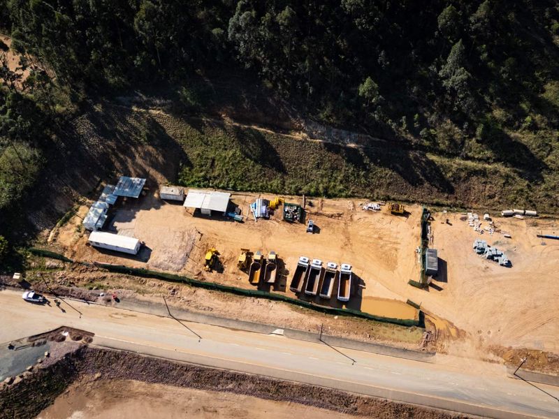 Aerial view of an industrial site featuring an unpaved yard, temporary structures, and perimeter fencing adjacent to a public road.