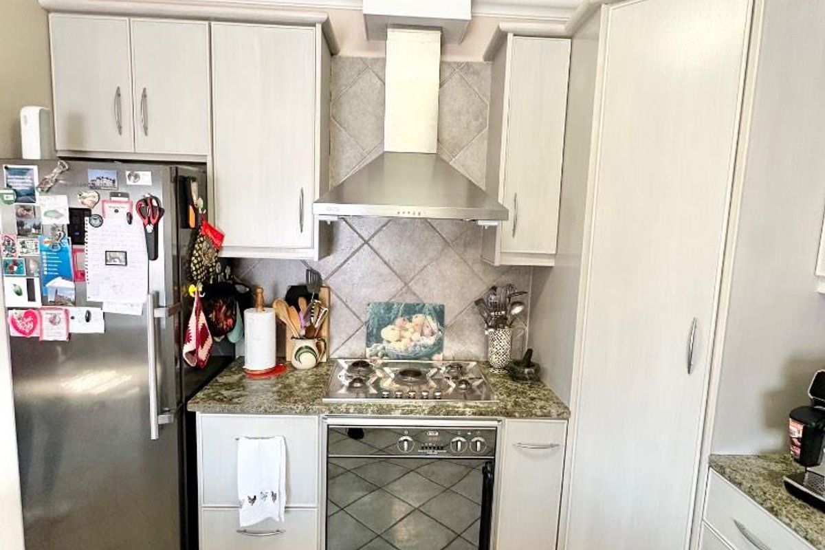 A functional kitchen featuring light-toned cabinetry, granite countertops, a built-in oven, gas hob, stainless steel extractor fan, and tiled flooring.