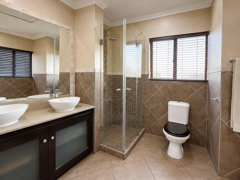 A well-maintained bathroom featuring a double vanity with vessel sinks, a glass-enclosed shower, and neutral-toned tiled walls and flooring.