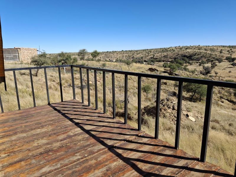 An elevated timber balcony featuring a metal balustrade, offering expansive views over the surrounding natural landscape.