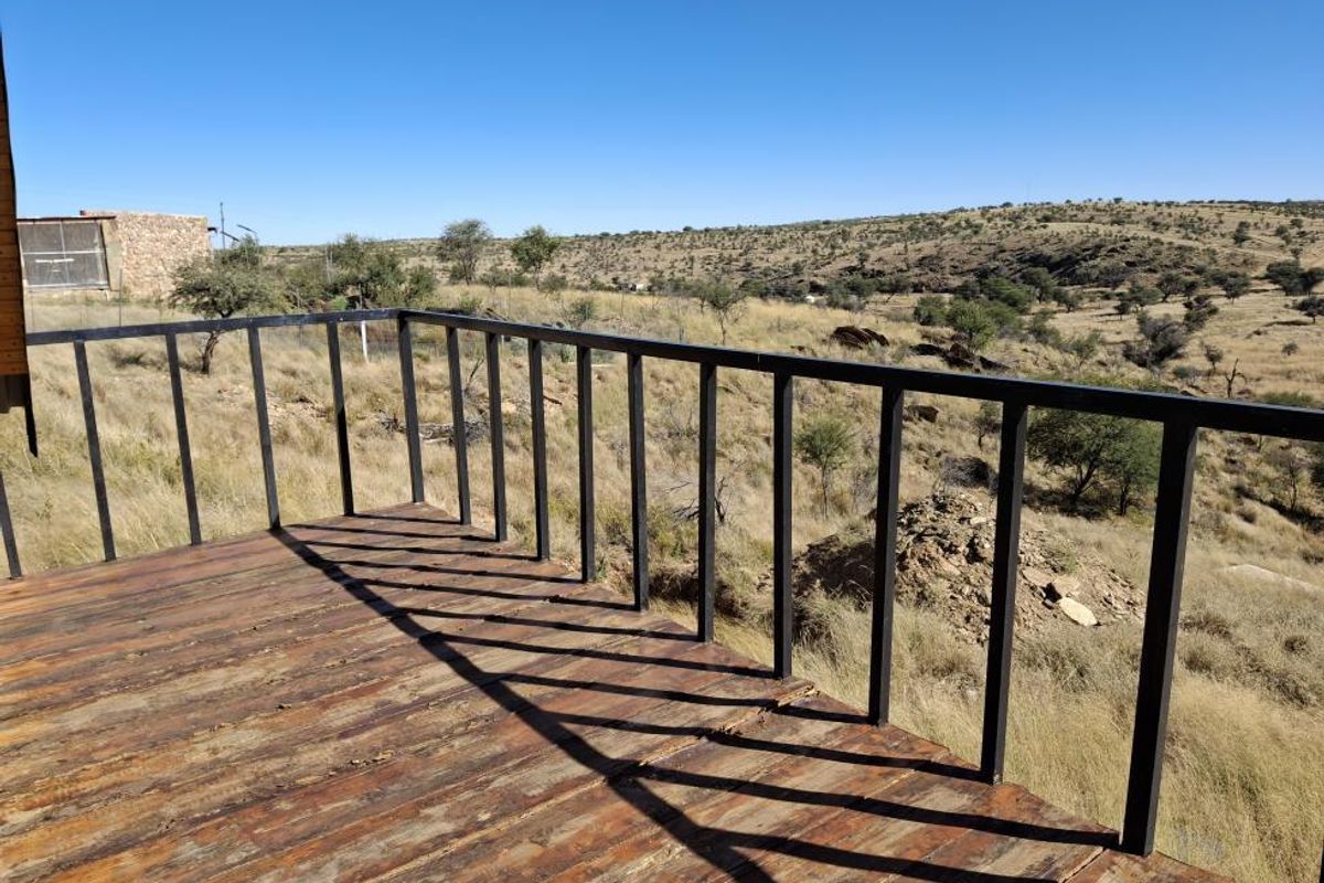 An elevated timber balcony featuring a metal balustrade, offering expansive views over the surrounding natural landscape.