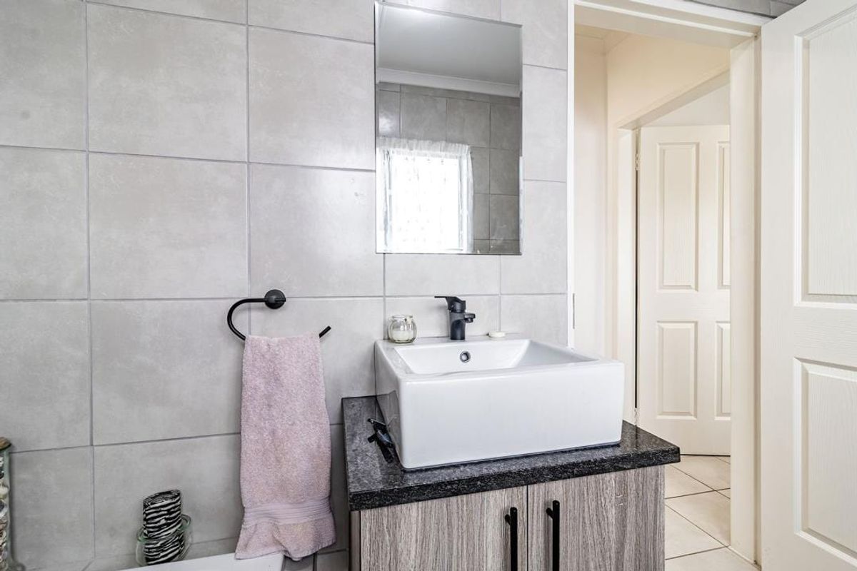 A modern bathroom featuring a vessel sink on a granite countertop with a vanity cabinet and neutral wall tiling.