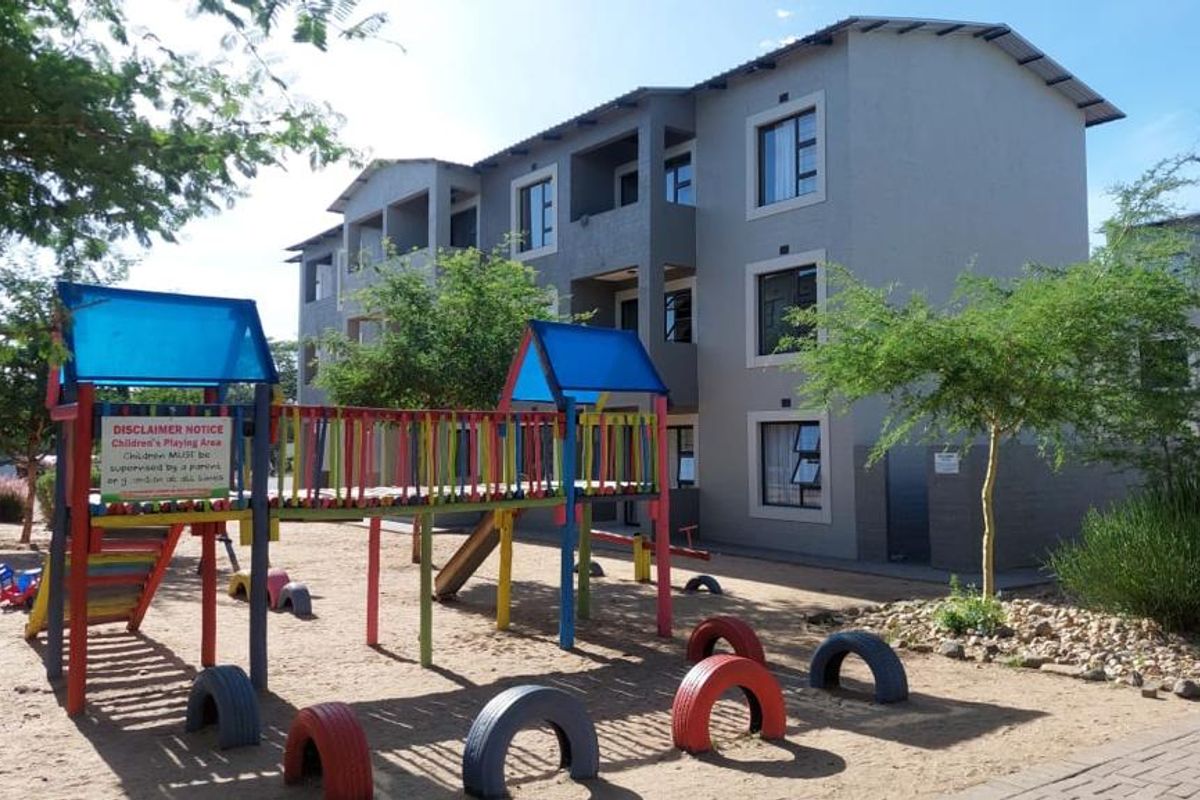 Exterior view of a multi-story apartment complex featuring a communal playground area with fixed play equipment and landscaped surroundings.