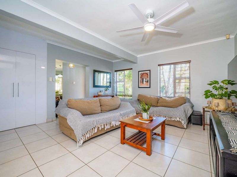 A bright living room featuring neutral tiled flooring, a ceiling fan, and built-in storage, offering a clean and functional space.