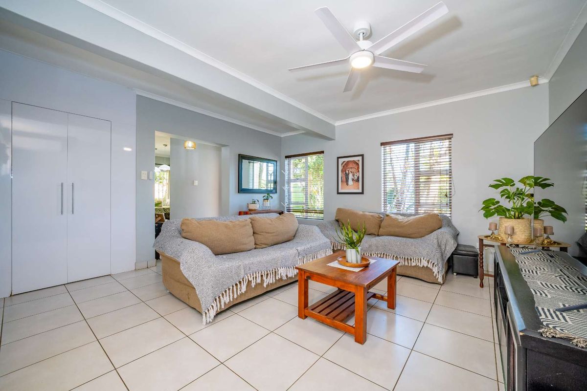 A bright living room featuring neutral tiled flooring, a ceiling fan, and built-in storage, offering a clean and functional space.