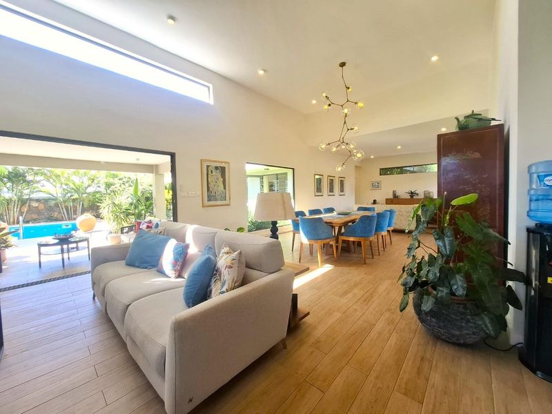 Spacious open-plan living and dining area featuring wood-look tile flooring, high ceilings with recessed lighting, and large sliding doors opening to the pool area.