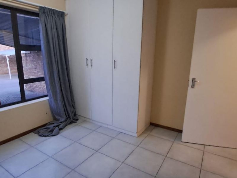A bright, empty bedroom featuring tiled flooring, built-in cupboards, and a large window overlooking the exterior parking area.