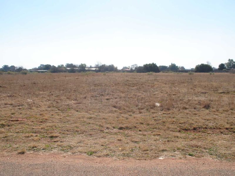 A wide-angle view of a flat, vacant residential plot of land with dry grass and surrounding vegetation.