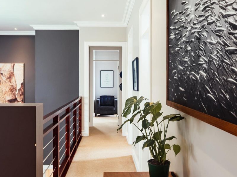 A well-maintained interior hallway featuring a wooden balustrade, neutral carpeting, and recessed ceiling lighting, providing access to adjacent rooms.