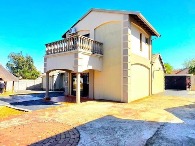 Rear view of the property featuring a paved courtyard, a balcony with balustrades, and a detached thatched lapa area.